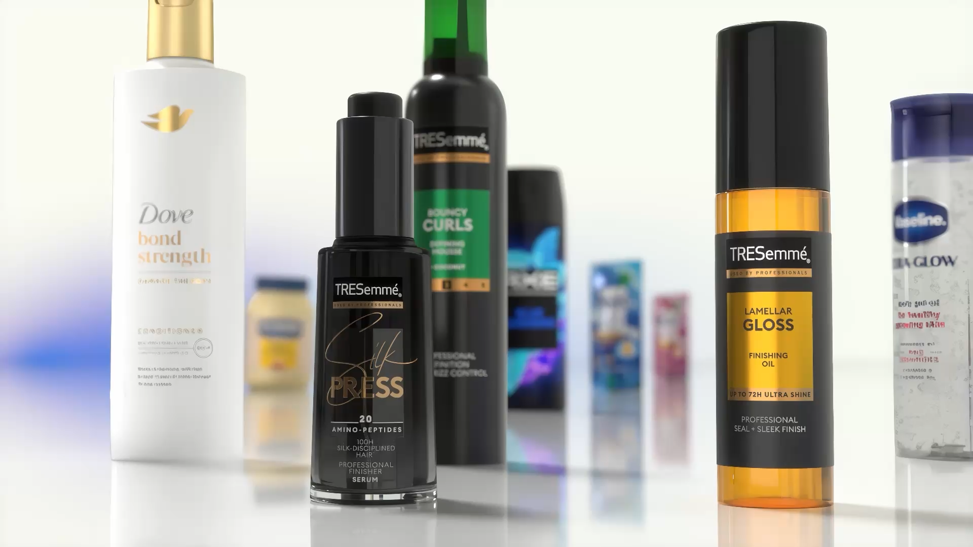 Detailný záber na rôzne produkty starostlivosti o vlasy a telo vystavené na reflexnom povrchu. Medzi viditeľnými položkami sú kondicionér Dove Bond Strength, sérum TRESemmé Silk Press, vrchný olej TRESemmé Lamellar Gloss a ďalšie produkty Unilever v pozadí.